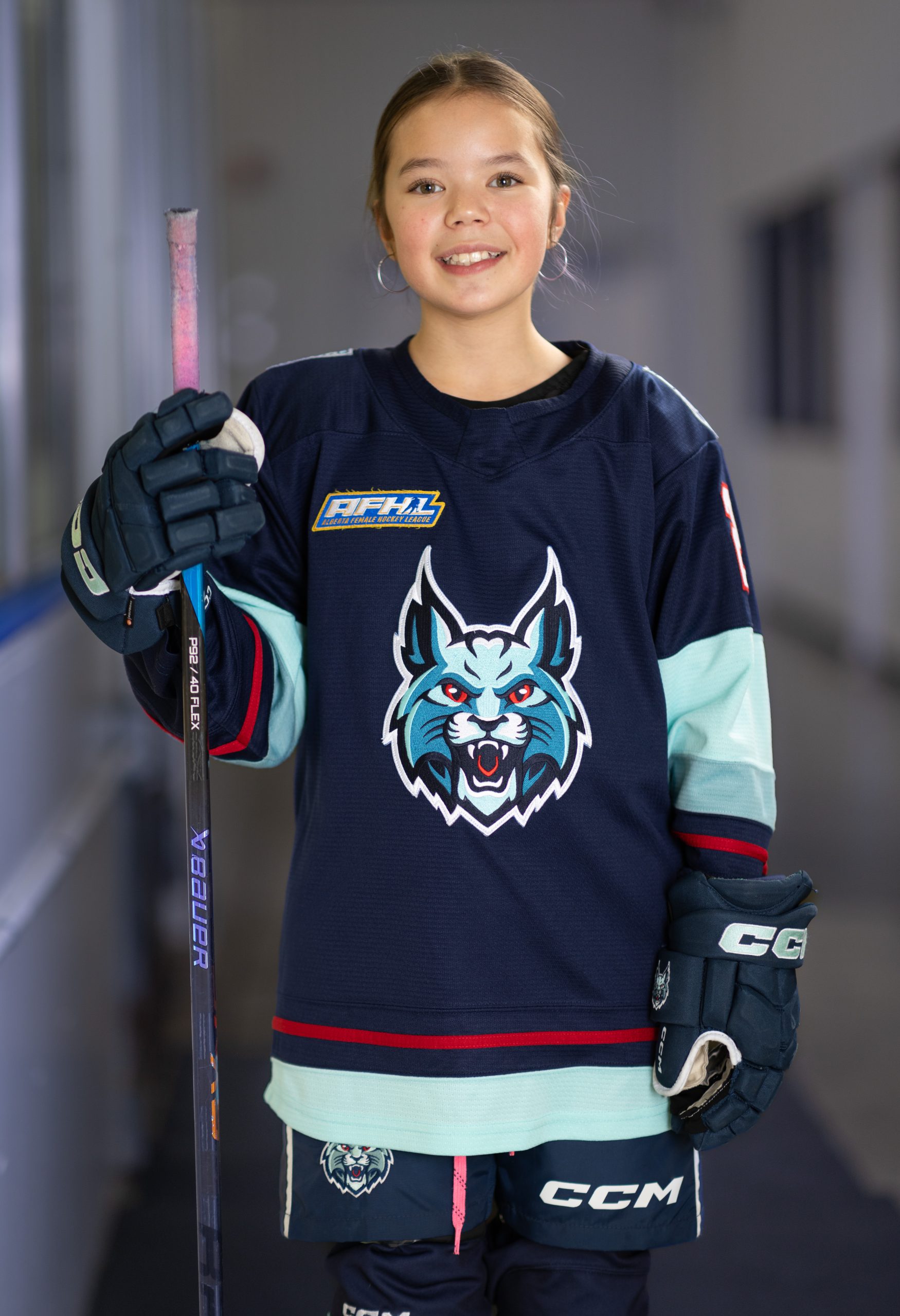 A 12 year old girl in a dark blue hockey uniform with a wolf crest, holding a hockey stick.