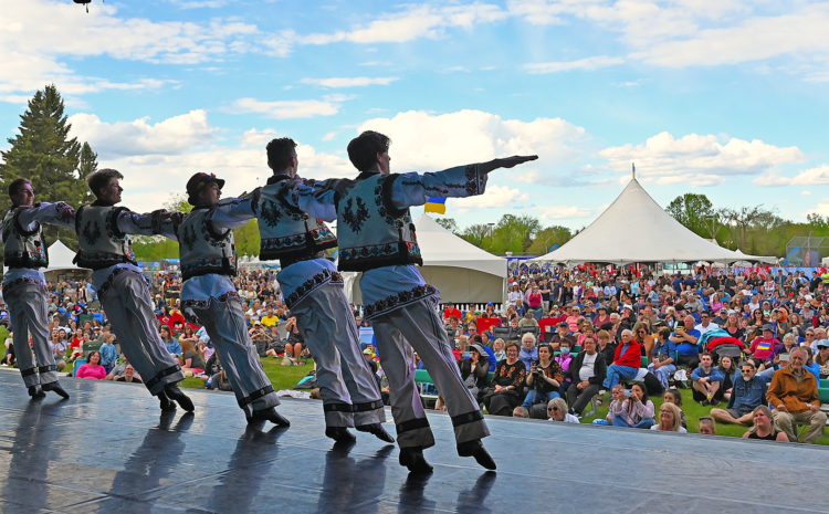 Ukrainian dancers perform on a stage in front of a large crowd at a summer festival.