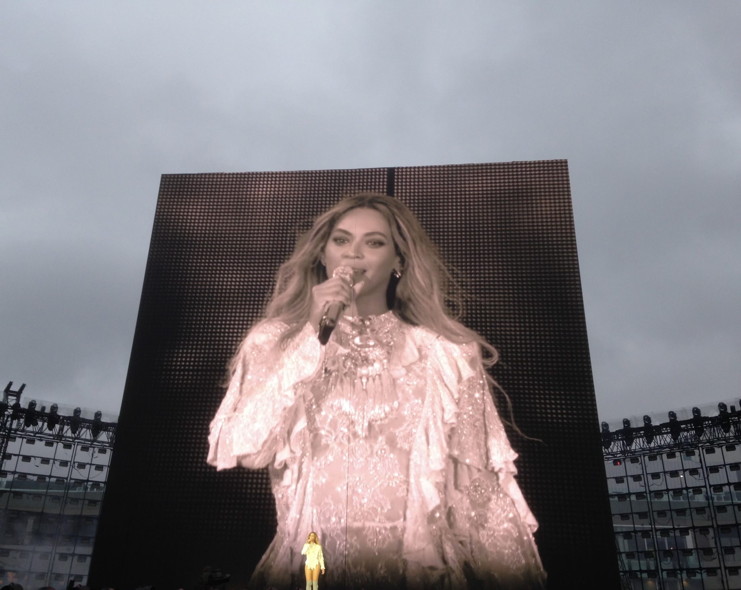 Beyoncé stands on stage in front of a live image of herself broadcast on a screen behind her.
