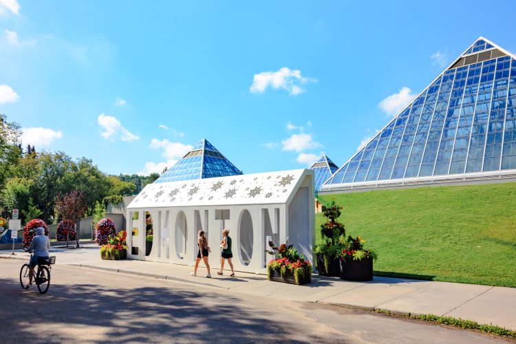 A large white metal sign with EDMONTON cut outs sits in front of glass pyramid buildings.