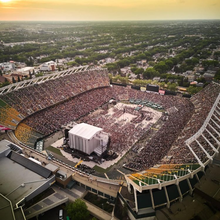 An aerial daylight shot of Commonwealth Stadium with fans standing in front of the stage and sitting in their seats in the stands.