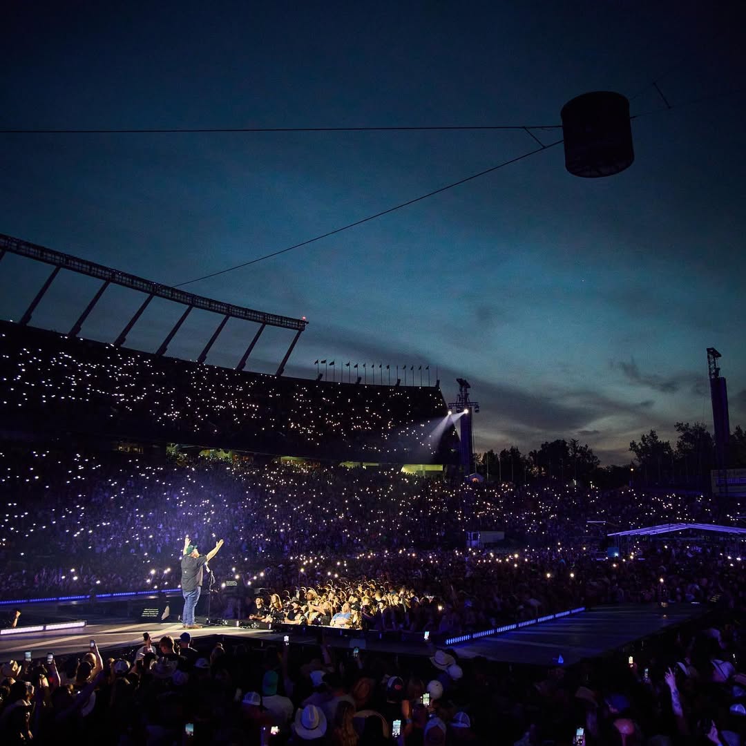 Under a night sky, Luke Combs performs on stage with thousands of fans and cell phones lit up around him.