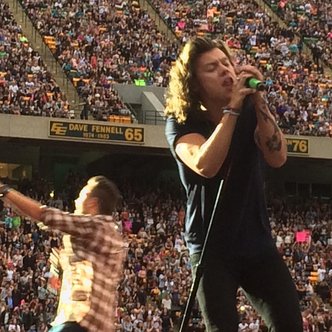 Harry Styles holds a microphone with both hands as he sings into it.