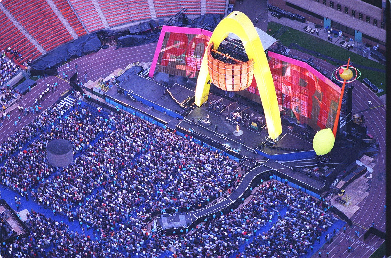 An aerial shot of thousands of fans sitting in front of a stage with a large yellow arch on it.