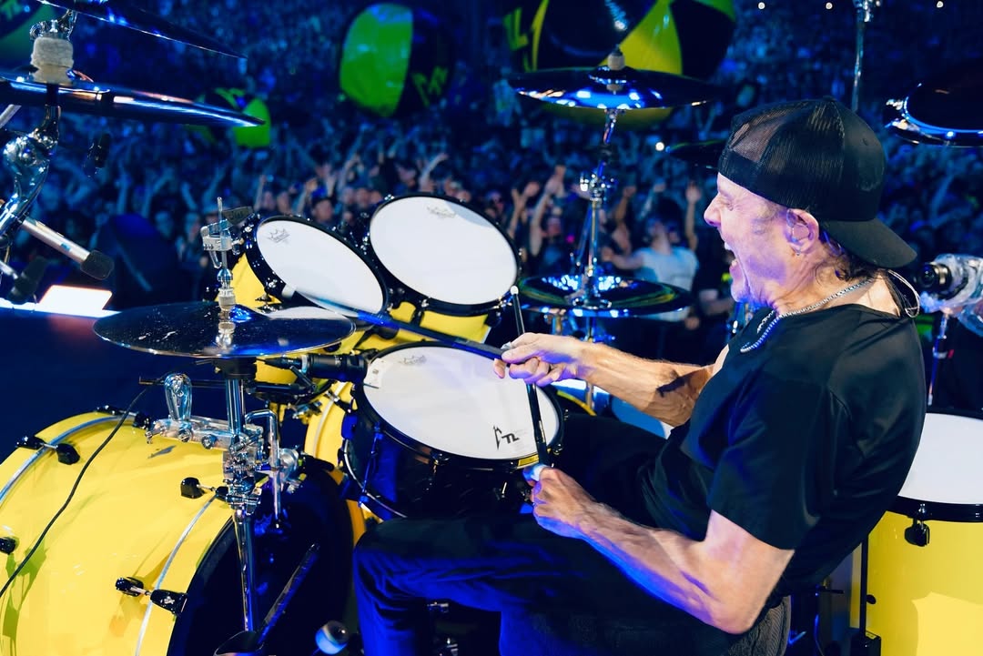 Lars Ulrich sits behind his drum kit and plays the drums.