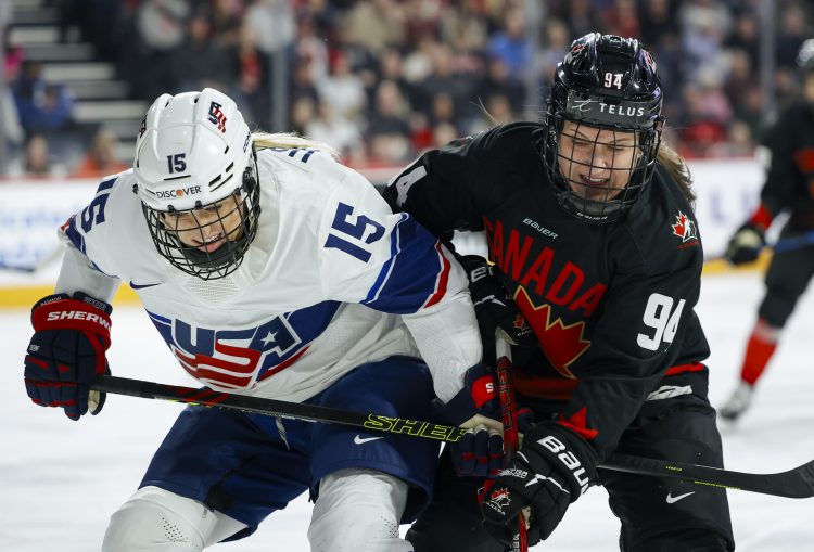 Two women, one in a white USA uniform and the other in a black Canadian uniform, playing ice hockey.