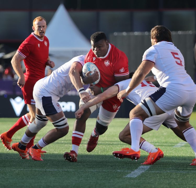 Male rugby players, representing Canada in red and USA in white, clash on an outdoor field