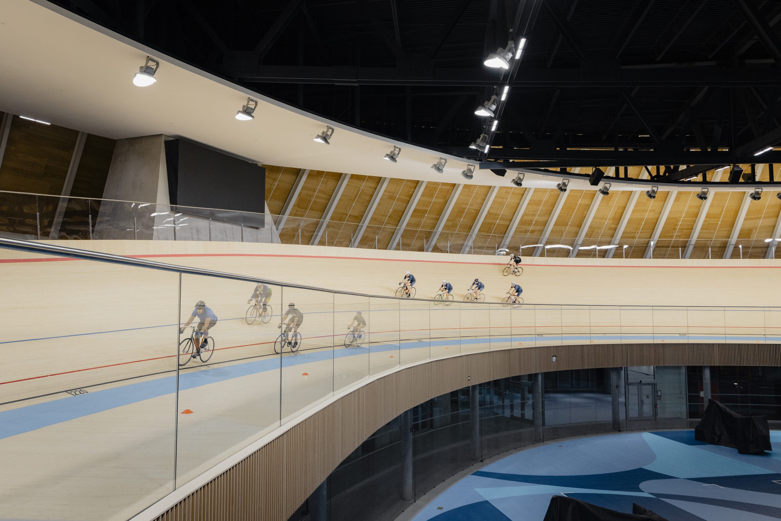 Two groups of cyclists ride on the wooden track of an indoor velodrome.