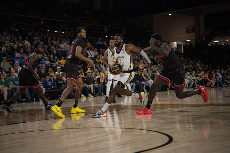 Four basketball players from two teams race down the court in front of a crowd. CR_Stingers