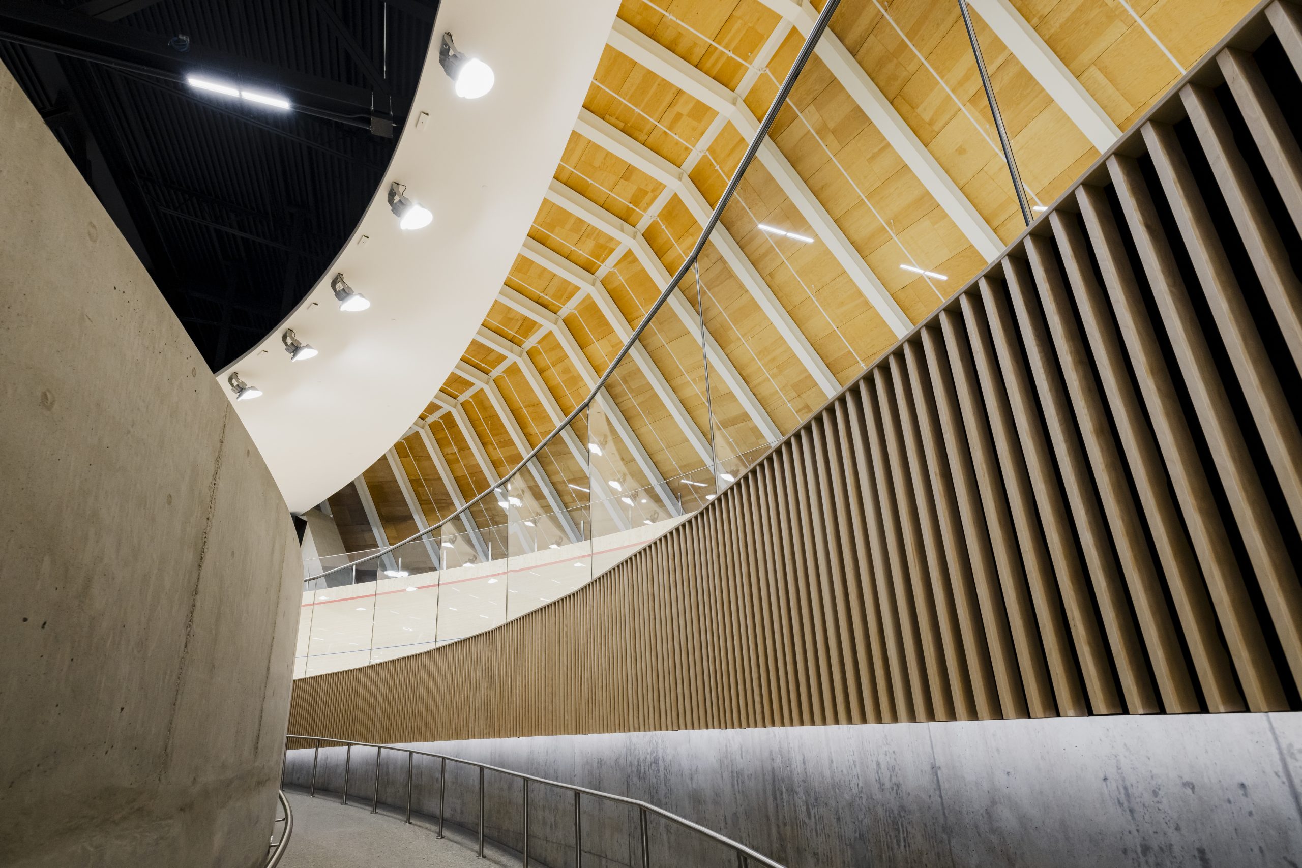 A curvilinear ramp, made out of concrete, leads up to a wooden indoor cycling track.