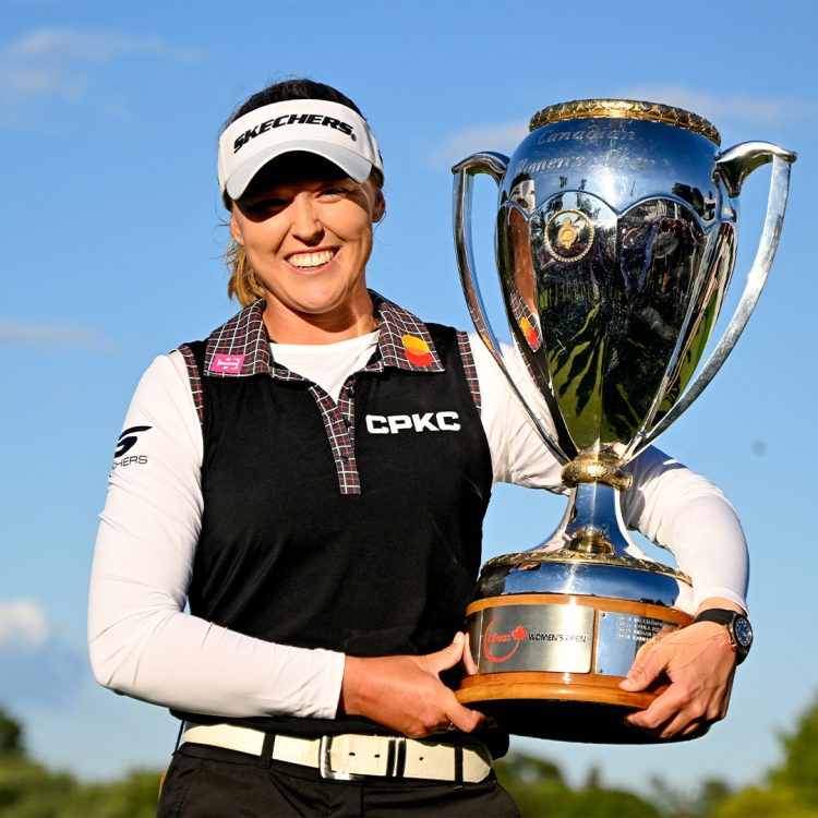 A woman holding a large golf trophy smiling at the camera.