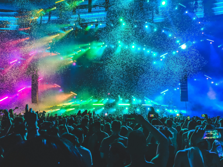 A crowd at a music festival with vibrant rainbow lights and confetti.